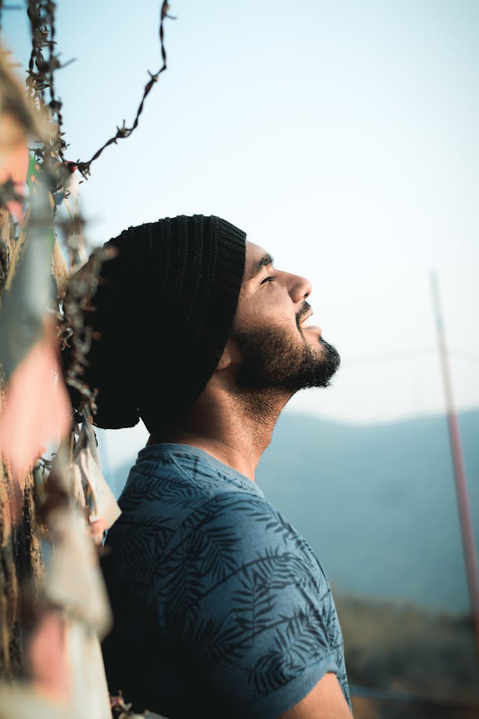 Side view of a serene man with a beard and hat, enjoying peaceful moment outdoors.