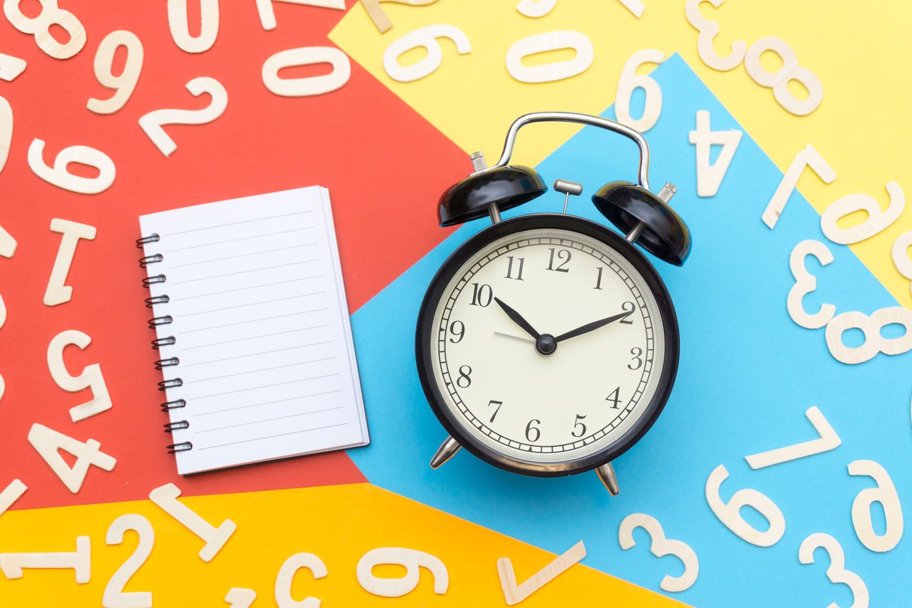 Creating a Daily Routine for Mental Health Recovery A flat lay of a classic alarm clock with a blank notebook on a colorful background surrounded by numbers.