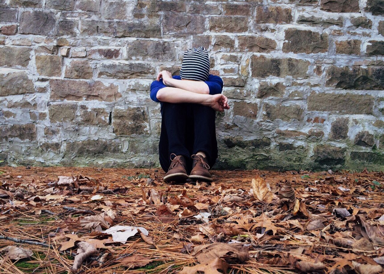 Signs It Is Time to Seek Depression Therapy A solitary figure sits against a stone wall surrounded by fallen leaves, expressing isolation.