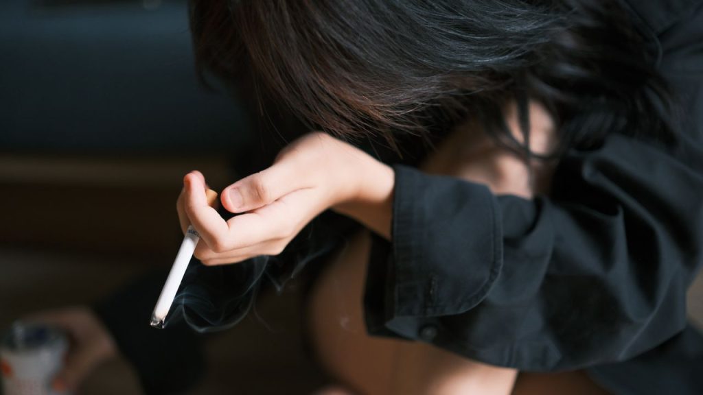 Close-up of a young woman holding a cigarette, indoors in a contemplative pose.