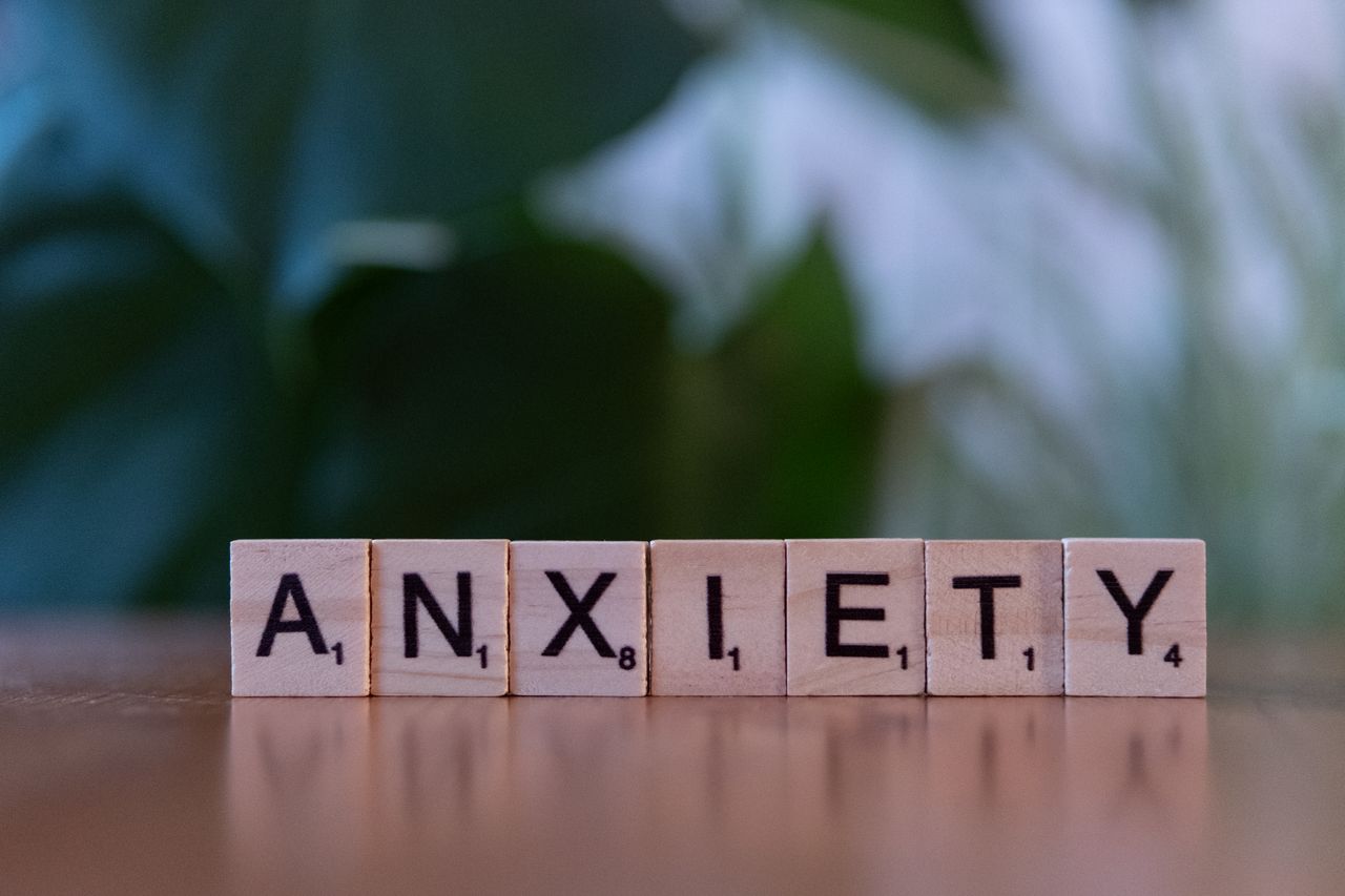 Close-up of wooden blocks spelling ANXIETY on a wooden surface with blurred green background.