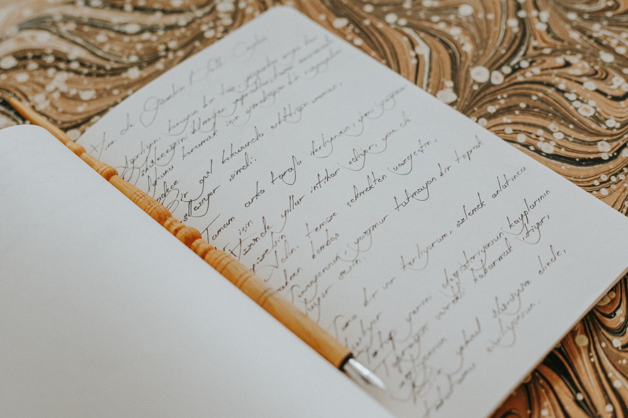 Open notebook with elegant handwriting placed on a marbled patterned surface, emphasizing creativity and artistry.