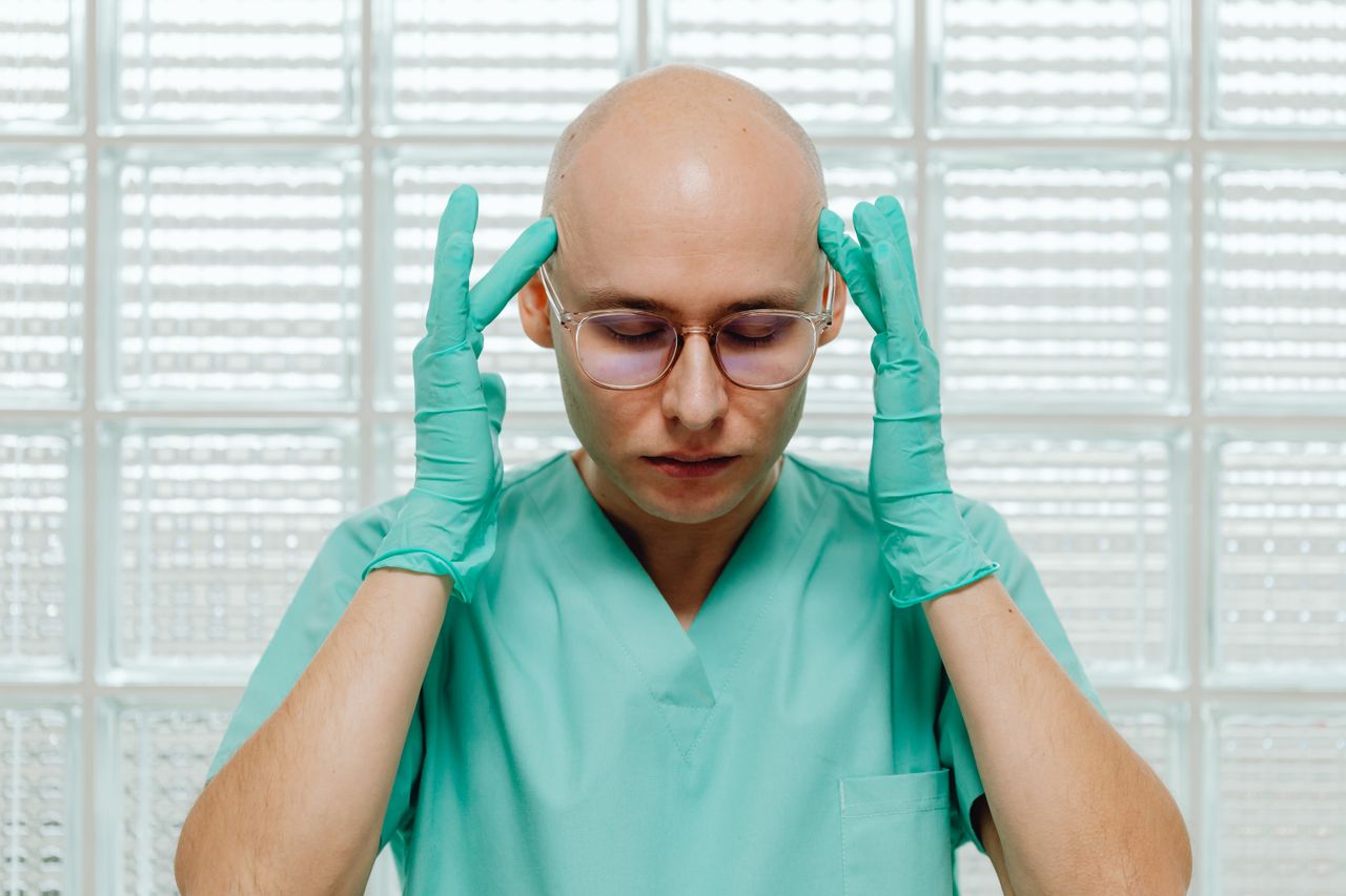 Fresh Paths to Healing: Modern Mental Health Practices in Addiction Recovery A surgeon in green scrubs appears stressed, holding their head with gloved hands indoors.