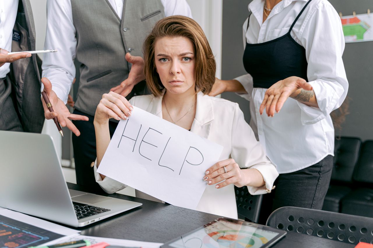 Healthy Ways to Manage Stress in Addiction Recovery Stressed office worker holding a help sign surrounded by colleagues' demands.