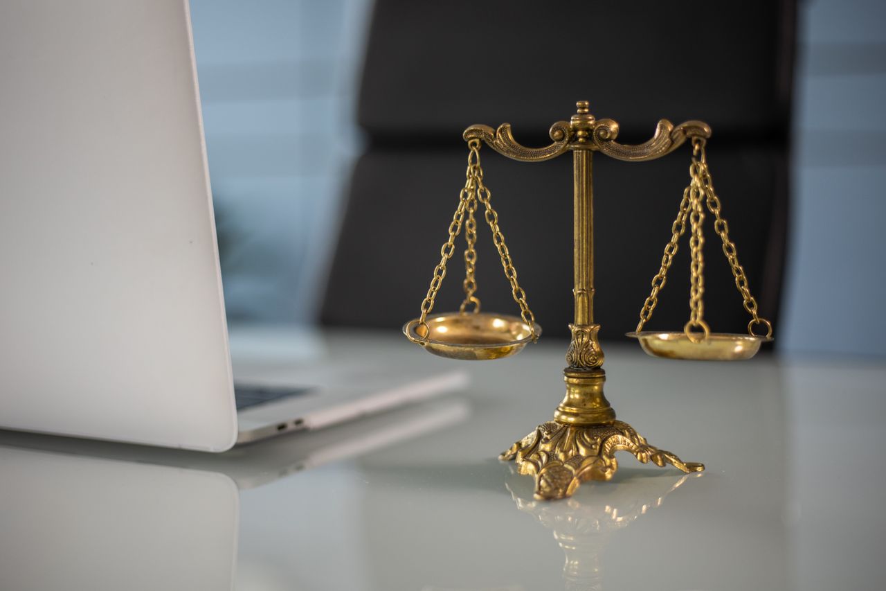 Questions to Ask When Choosing PHP vs IOP Treatment Golden justice scales on a desk beside a laptop, symbolizing law and balance.