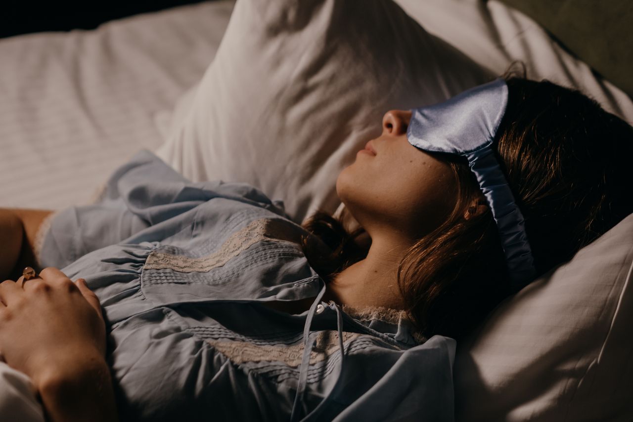 How Screen Time Affects Student Sleep and Mood A woman peacefully sleeping with a blue eye mask in a dimly lit room.